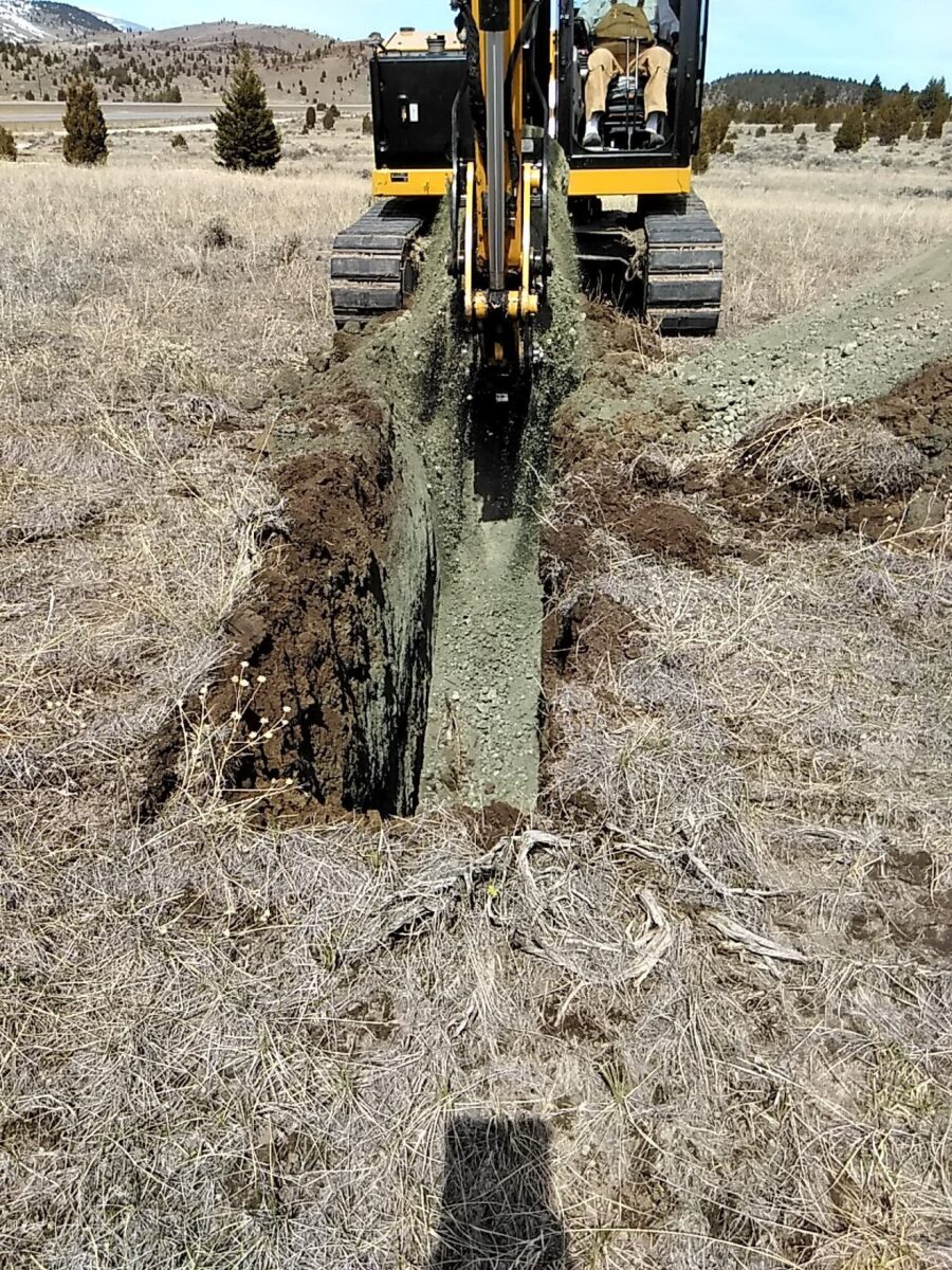 Excavator digging trench in dry field.